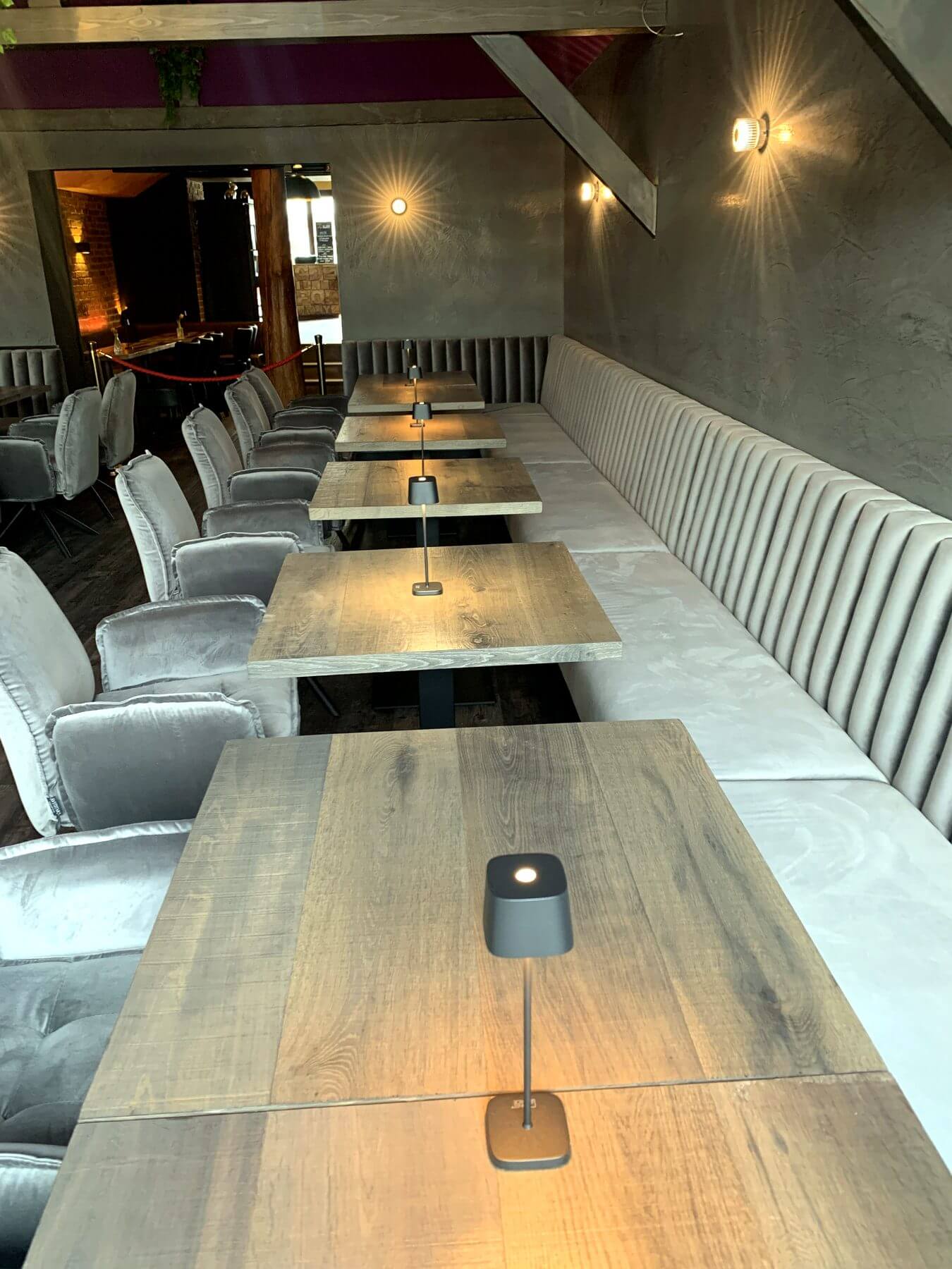 Loungebereich mit Holztischen im Die2 Neubiberg Loungebereich im Die2 Neubiberg mit langen Holztischen, heller Polsterbank und stimmungsvoller Wandbeleuchtung