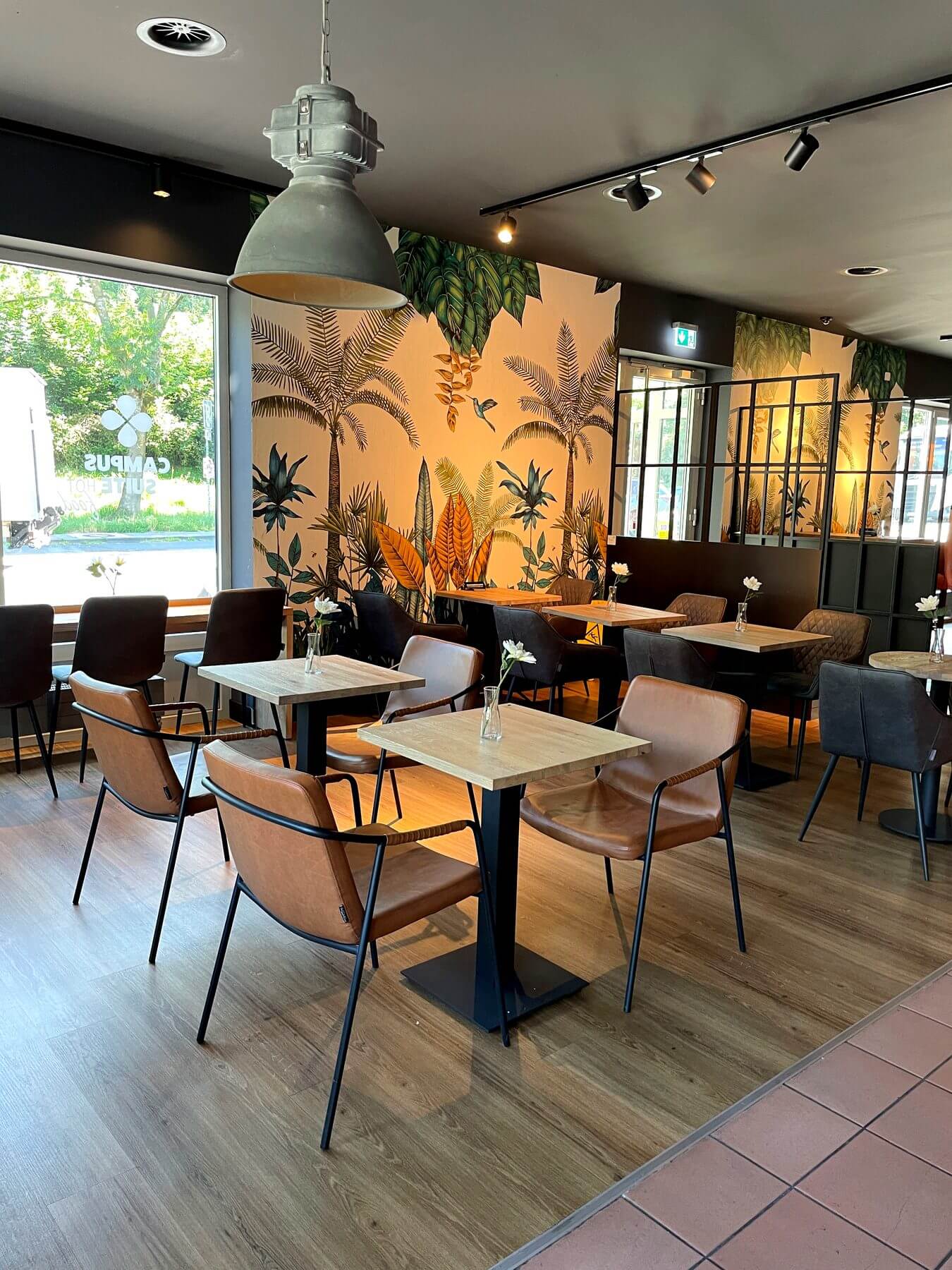 Café-Einrichtung im Coffee Fellows Sitzbereich Sitzbereich bei Coffee Fellows Campus Suite mit kompakten Tischen, Stühlen und dekorativer Wandgestaltung