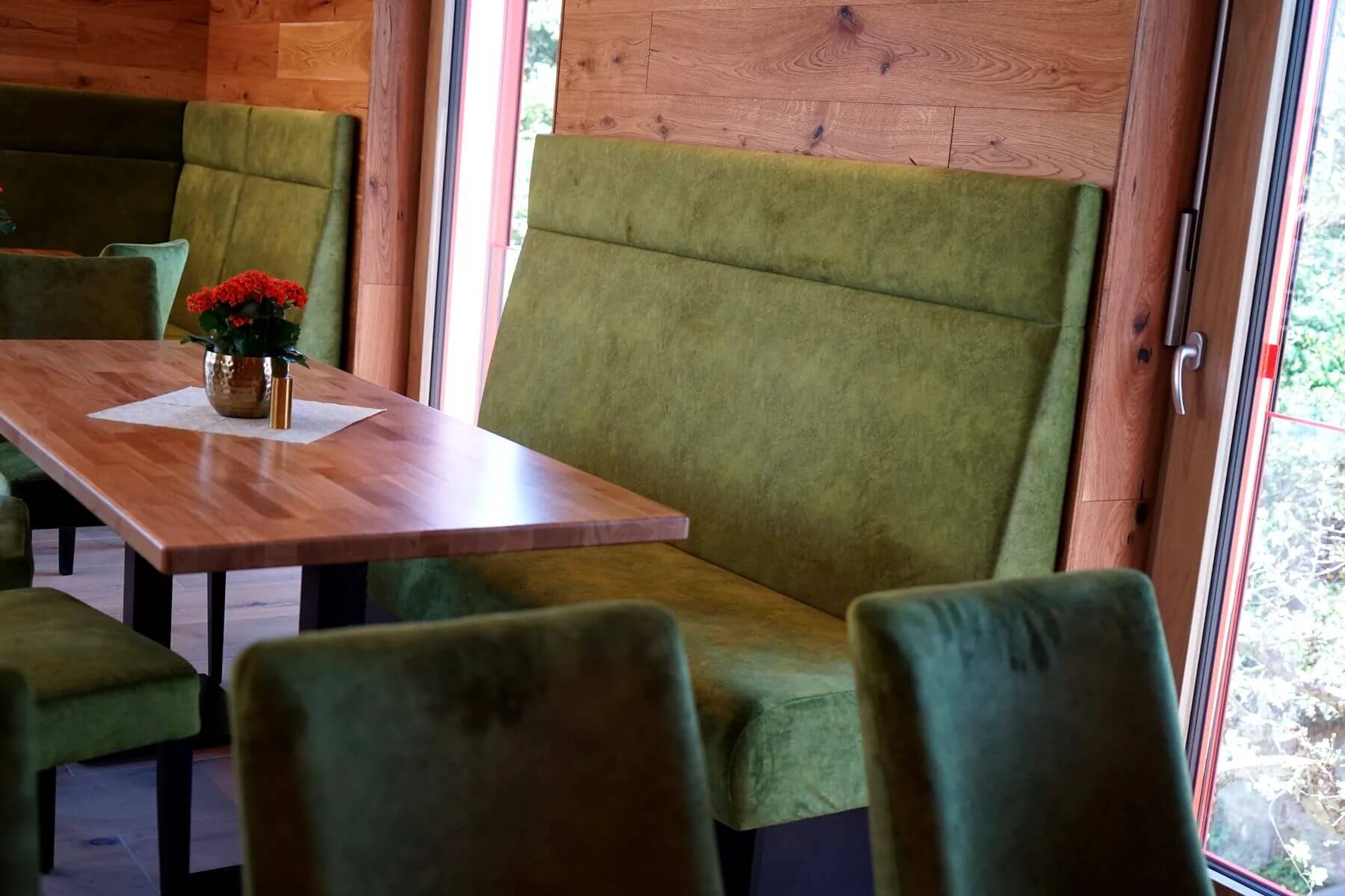 Tischdekoration und Polsterbank im Cafe Flow Holztisch mit Blumendekoration vor gruener Polsterbank im Cafe Flow Marktgraitz