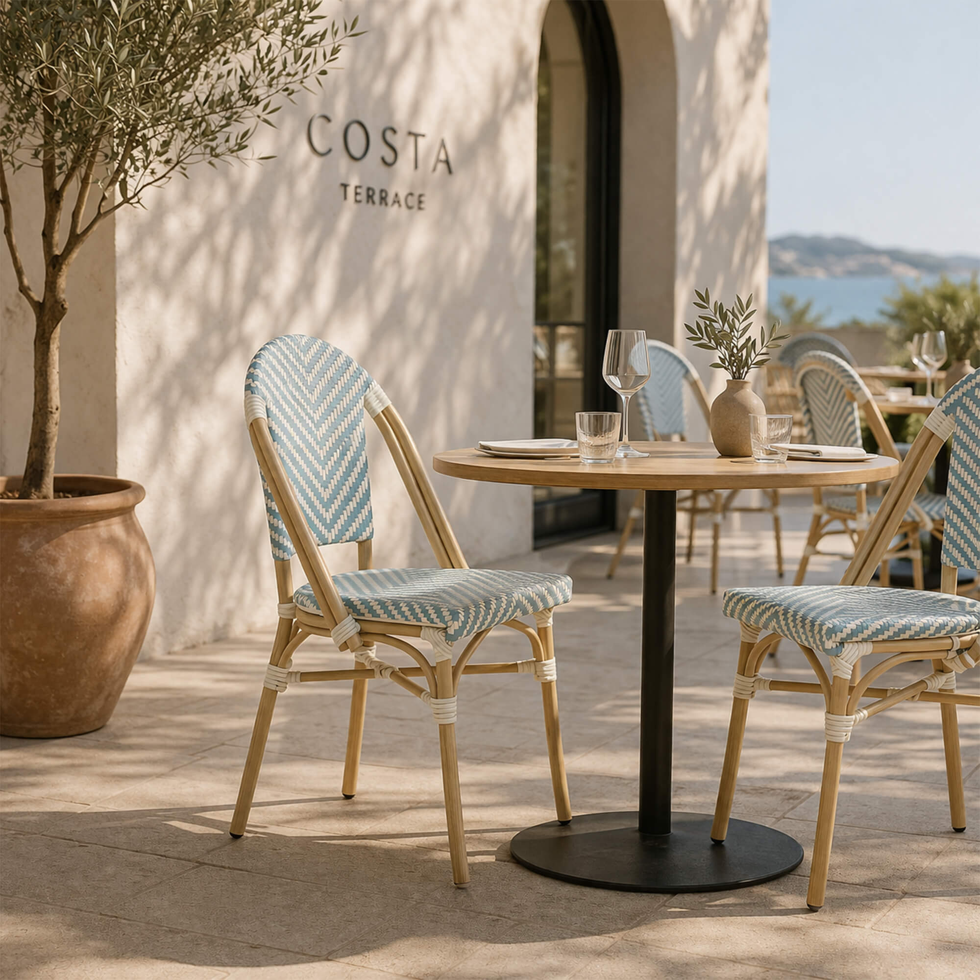 Outdoorstuhl Zypern Blue White auf Holzterrasse Outdoorstuhl Zypern – blau-weißer Bistrostuhl in Flechtoptik auf stilvoller Holzterrasse mit Blumen