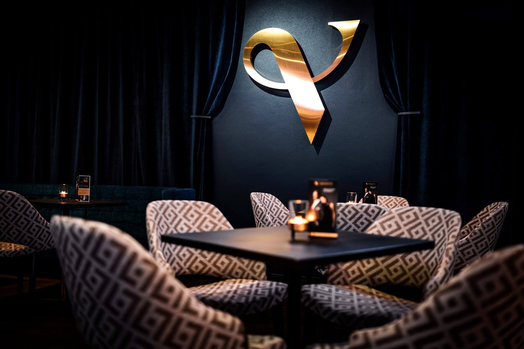Sitzgruppe vor Vorhang und Logo Sitzgruppe im Zaubertheater VERSCHMITTST vor dunklem Vorhang und goldenem Wandlogo