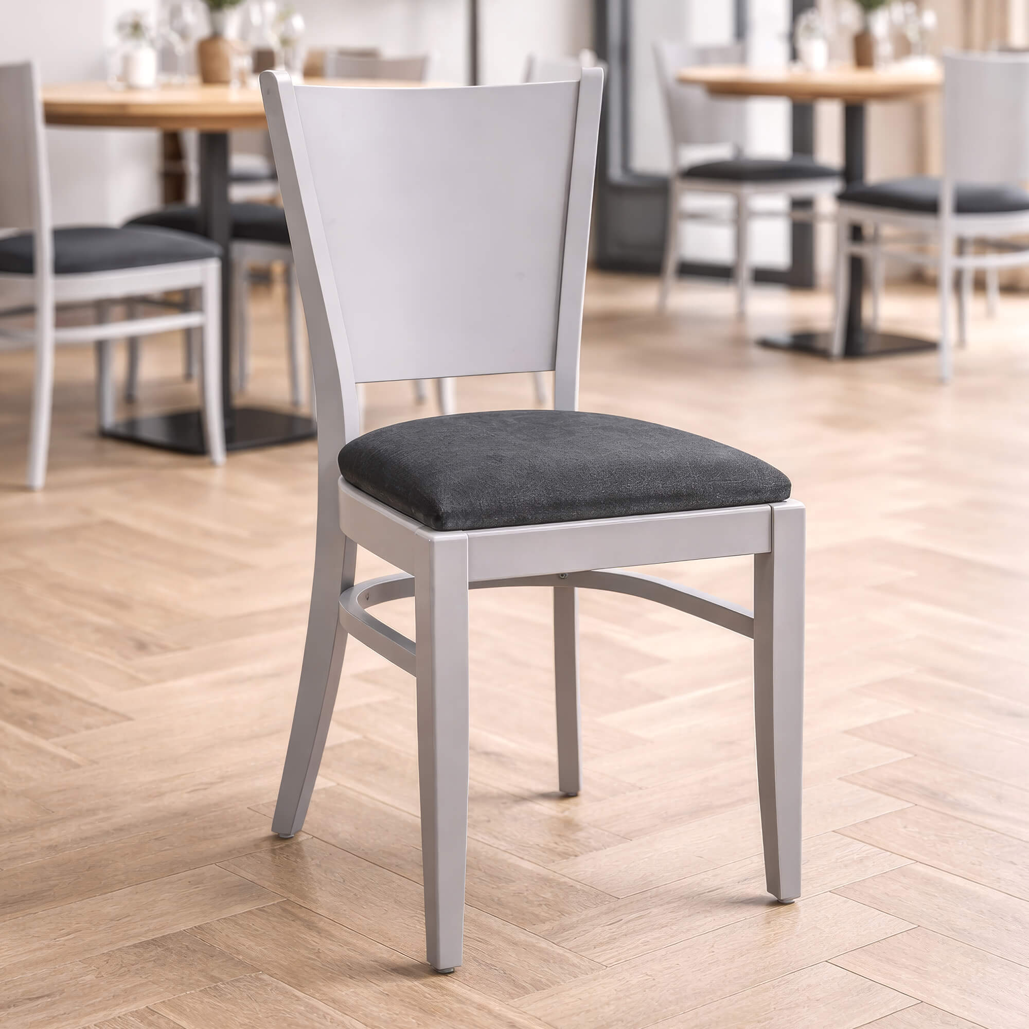 Holzstuhl Saravo P Grau als stilvoller Restaurantstuhl in heller Umgebung Holzstuhl Saravo P Grau mit grauer Polsterung und hellem Holzgestell in modernem Gastronomie-Innenraum