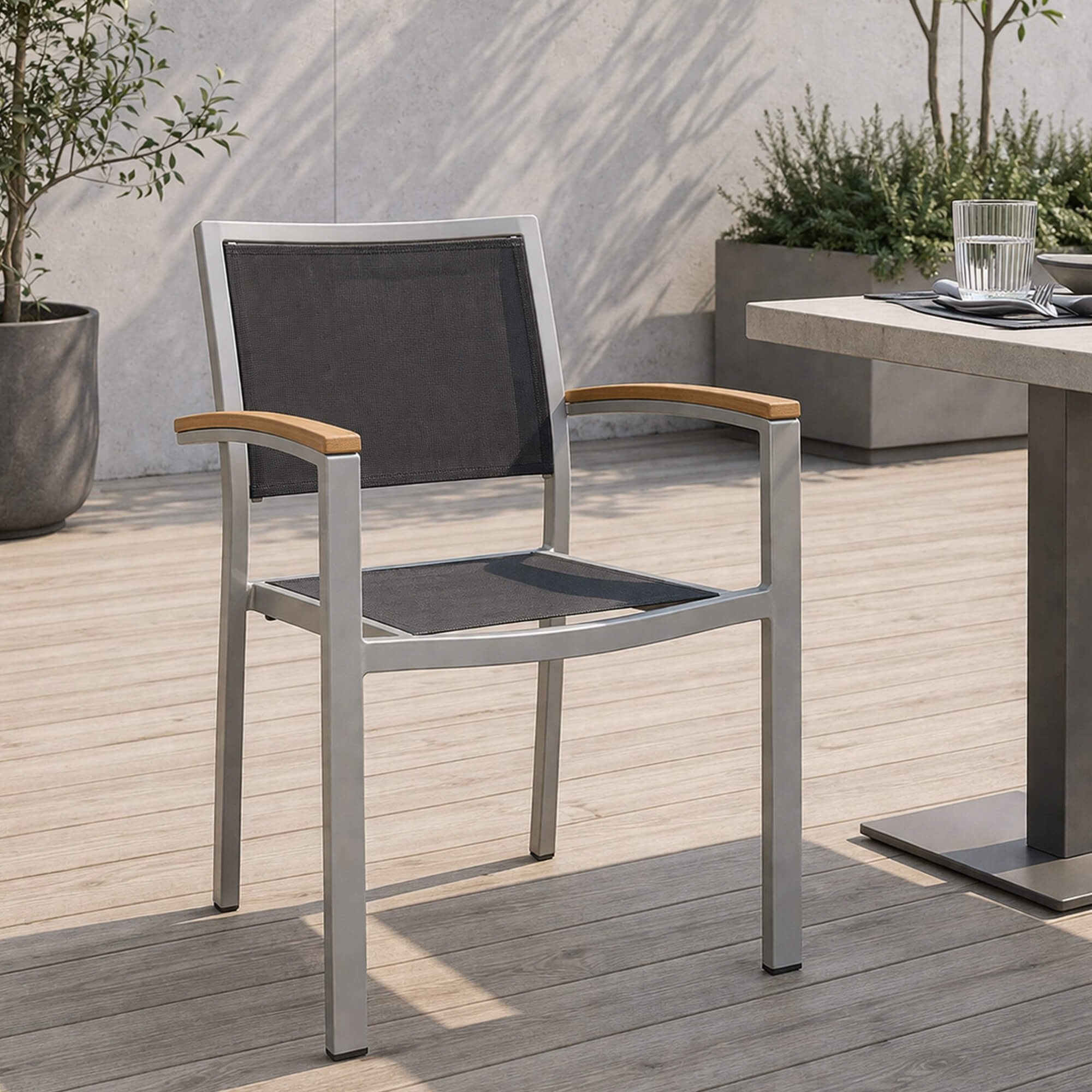 Outdoorstuhl Georgia – silber-schwarzer Outdoorstuhl mit Armlehnen vor Caféterrasse auf Kopfsteinpflaster