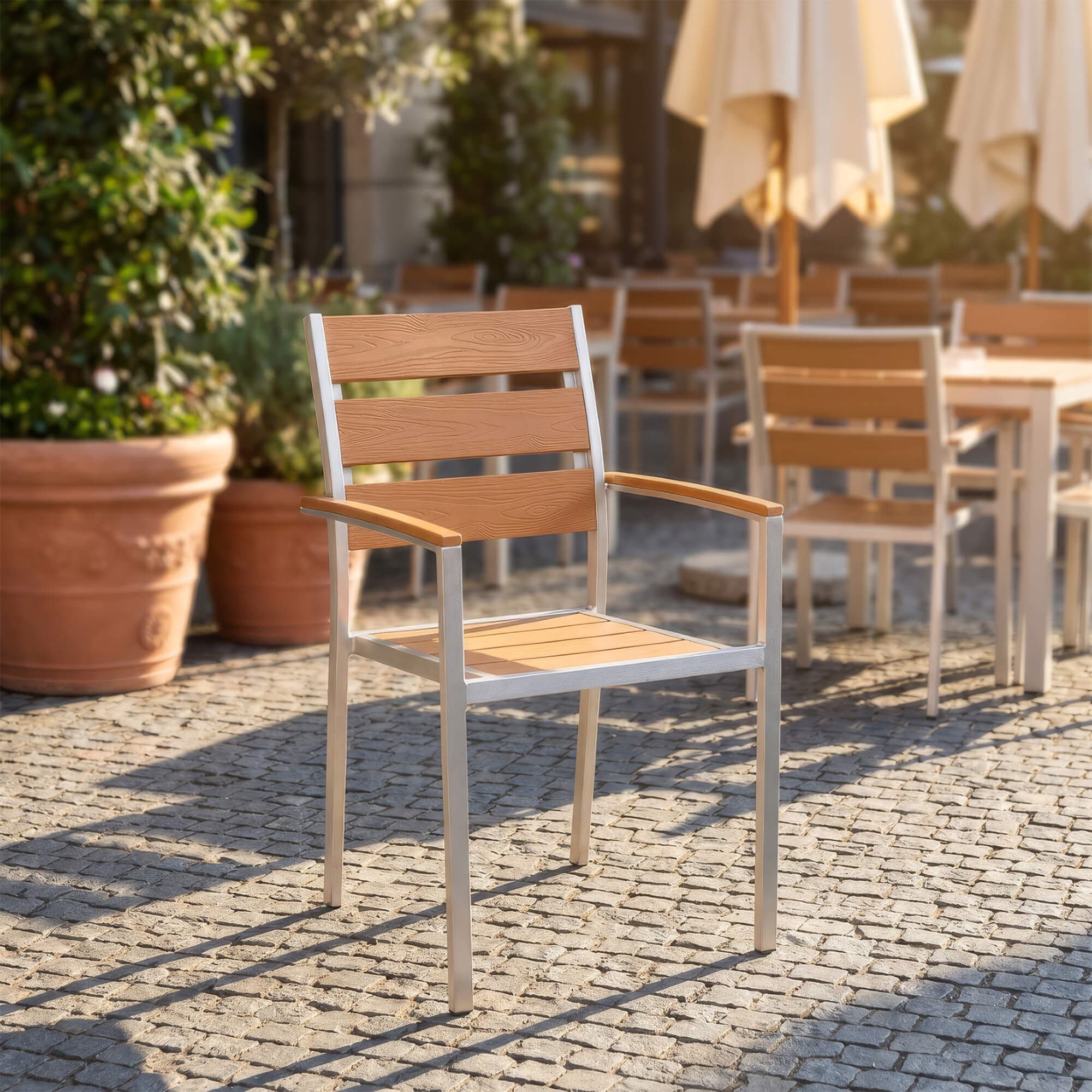 Stapelbarer Outdoorstuhl in Teak für Gastronomie-Terrassen Stapelbarer Outdoorstuhl in Teak mit Armlehnen auf gepflasterter Terrasse
