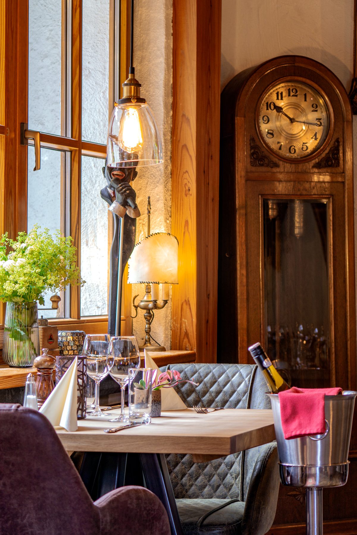 Fensterplatz im Alten Wohnzimmer der Eifeler Seehütte mit gedecktem Tisch, Pendelleuchten und Standuhr